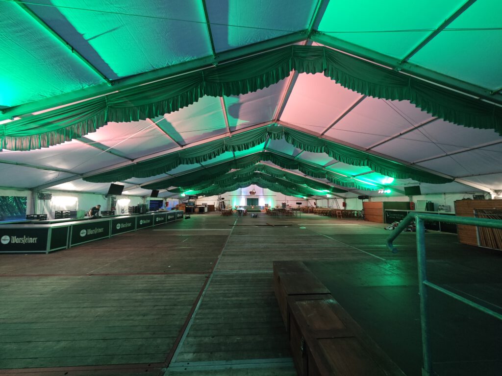 Grün beleuchtetes Festzelt mit Sitzplätzen und Ausschankbereich