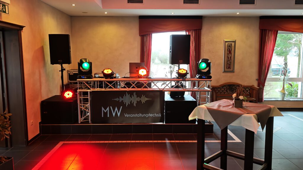 DJ-Pult mit MW-Banner, Lautsprechern und Lichttechnik im Veranstaltungsraum