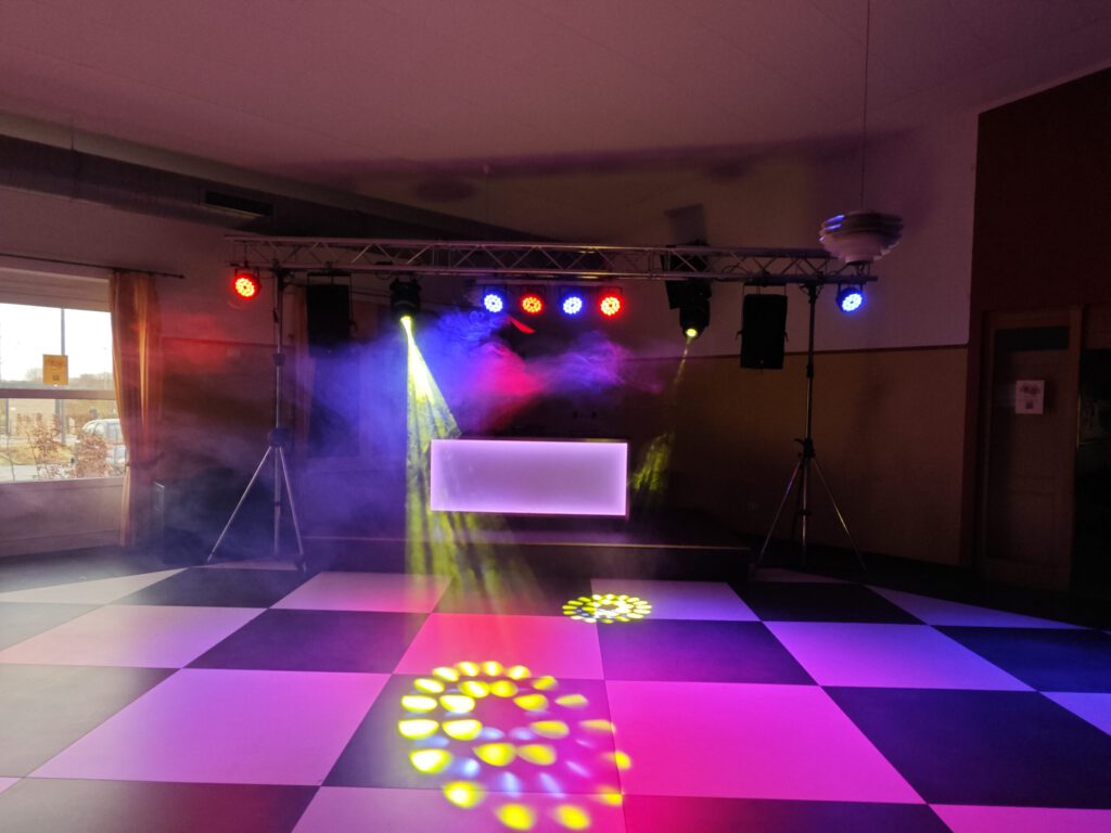 DJ-Pult mit Lautsprechern und farbigen Lichteffekten auf einer Tanzfläche