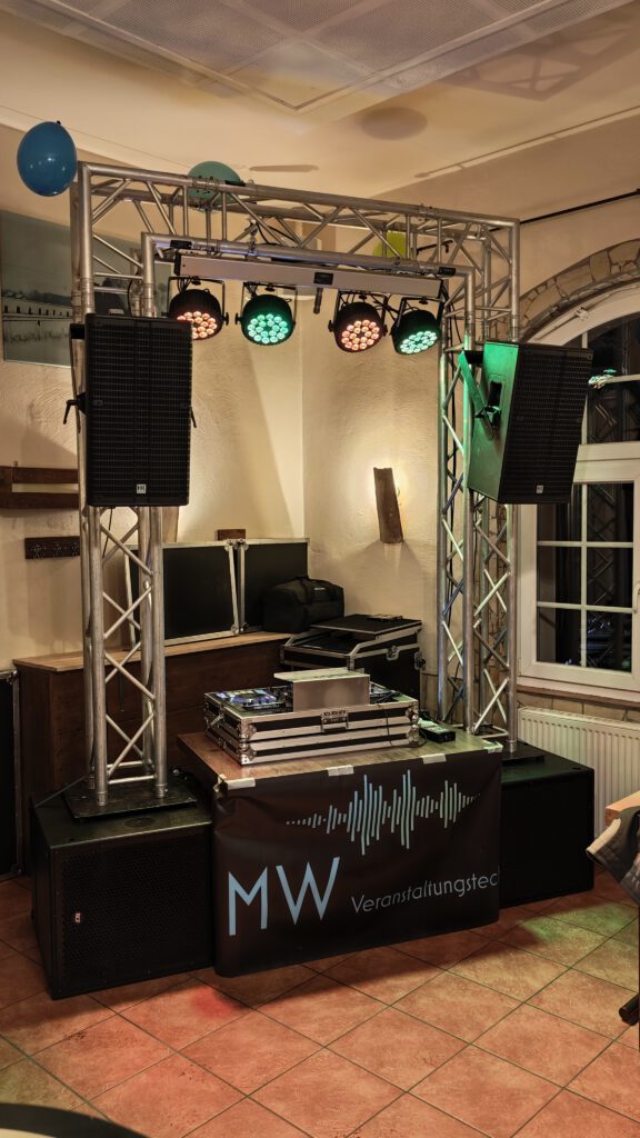 DJ-Pult mit MW-Banner und Lichttechnik in einem Innenraum